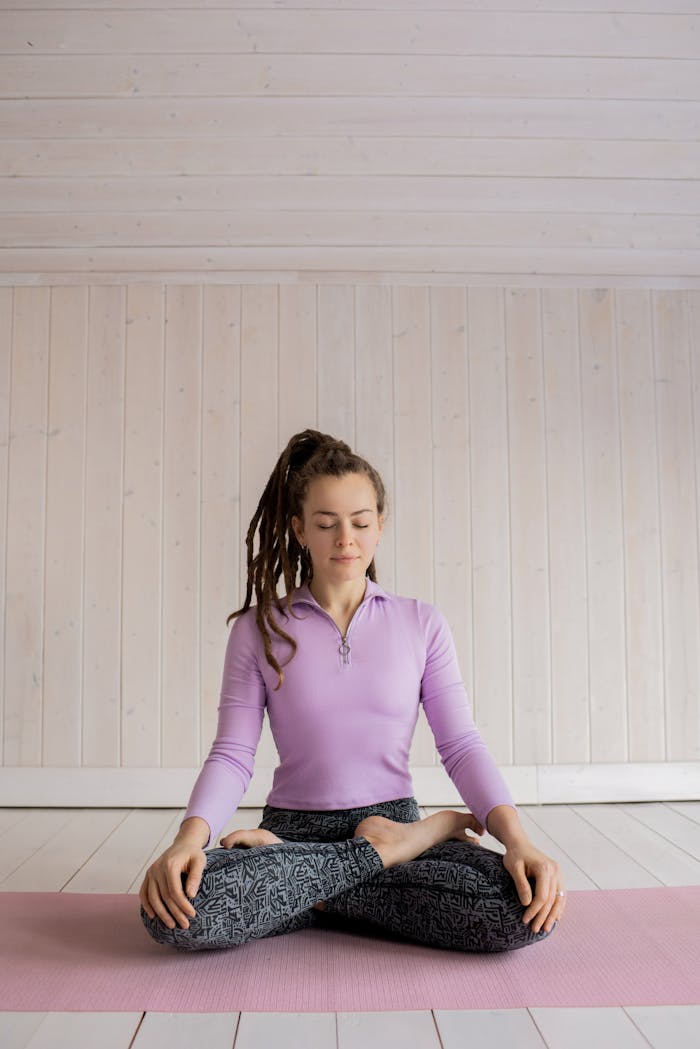 get-in-touch Woman practicing yoga meditation indoors on a pink mat, focusing on relaxation and mindfulness.